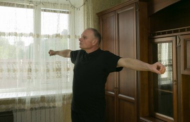 Sabah egzersizleri. Yaşlı bir adam evde jimnastik yapıyor. Karantina süresince tüm spor merkezleri kapalıdır..