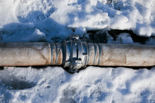 Winter. Everything is covered with snow. Leak in the connection of pipes pumping water out of the pond.