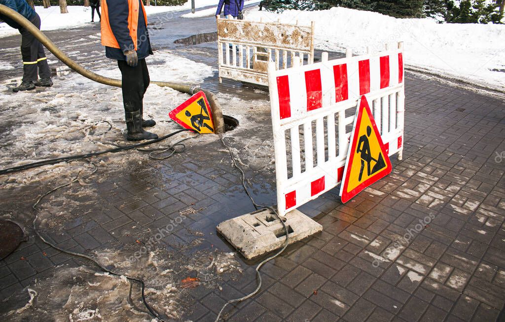Road works sign. The municipal service removes the blockage in the sewer hatch. Severe winter frosts set in.