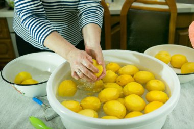 Evde limoncello limonata yapma süreci. Bir erkek ve bir kadın limonları bir kap suda yıkıyorlar..