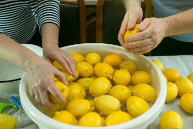 Evde limoncello limonata yapma süreci. Bir erkek ve bir kadın limonları bir kap suda yıkıyorlar..