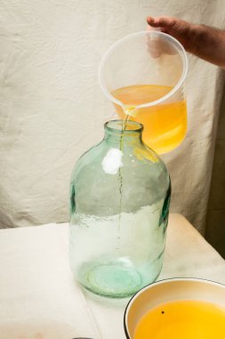Evde limoncello limonata yapma süreci. Bir adam limon aromalı filtrelenmiş alkolü on litrelik cam şişeye doldurur..