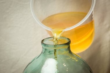 Evde limoncello limonata yapma süreci. Bir adam limon aromalı filtrelenmiş alkolü on litrelik cam şişeye doldurur..