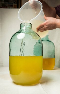 The process of making limoncello lemon liqueur at home. A man mixes lemon zest alcohol with sugar syrup in a ten-liter glass bottle. clipart