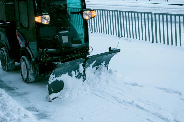 Snowplow removing snow on street after blizzard. Snowplow vehicle clears snowy road during blizzard. Snow clearing equipment. Tractor with snow plow blade clears road in city from fresh fallen snow.