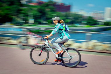 Hareket bulanıklığı. Genç bir kadın şehir seti boyunca bisiklet sürüyor..