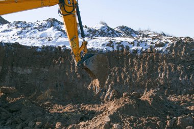 Sürüngen kazıcı. İnşaat alanında yer değiştiren bir makine. Çalışma sürecindeki kazıcı toprağı kazıyor ve araziye döküyor. Açık bir kış gününde çalışır..