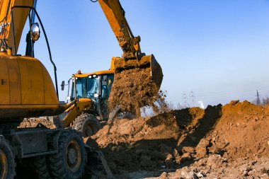 Sürüngen kazıcı. Çalışma sürecindeki kazıcı toprağı kazar ve araziye döker. Açık bir kış gününde mavi gökyüzüne karşı çalışır.