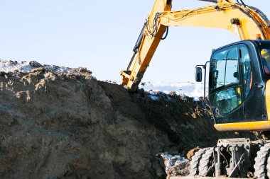 Sürüngen kazıcı. Çalışma sürecindeki kazıcı toprağı kazar ve araziye döker. Açık bir kış gününde mavi gökyüzüne karşı çalışır.