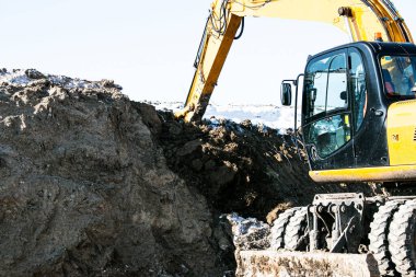 Sürüngen kazıcı. Çalışma sürecindeki kazıcı toprağı kazar ve araziye döker. Açık bir kış gününde mavi gökyüzüne karşı çalışır.