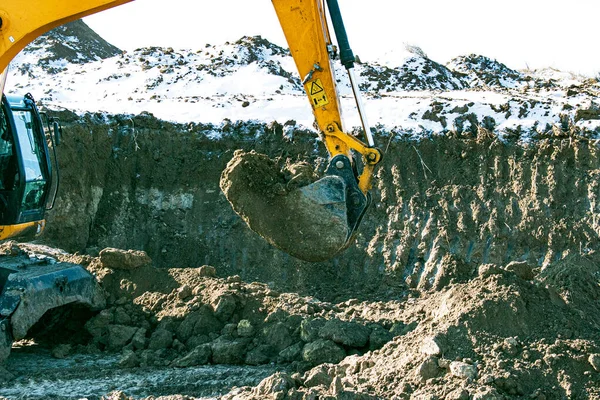 Crawler excavator. Earth-moving machine at a construction site. The excavator in the process of work digs up the earth and pours it onto the site. Works on a clear winter day.