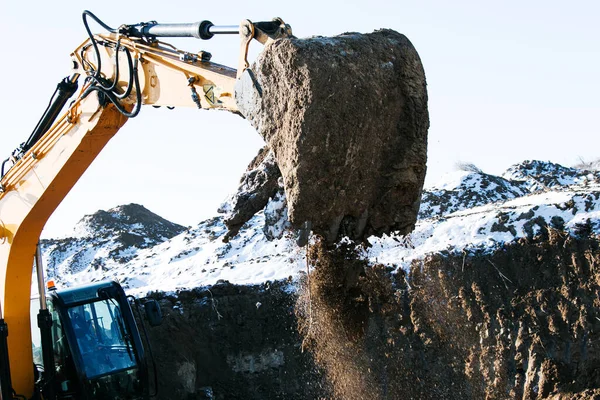 Crawler excavator. Earth-moving machine at a construction site. The excavator in the process of work digs up the earth and pours it onto the site. Works on a clear winter day.