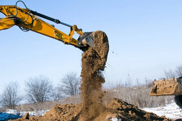 Crawler excavator. The excavator in the process of work digs out the earth and pours it onto the site. Works on a clear winter day against the blue sky.