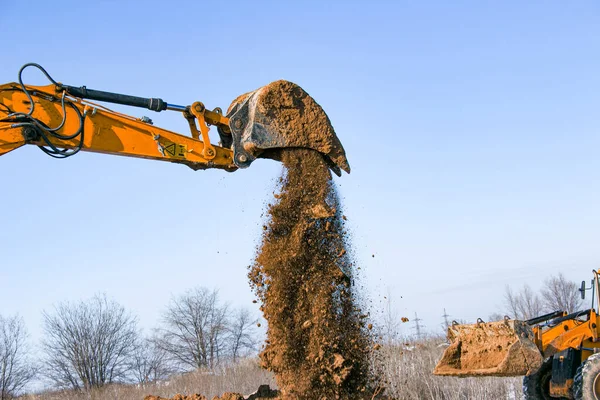 Crawler excavator. The excavator in the process of work digs out the earth and pours it onto the site. Works on a clear winter day against the blue sky.