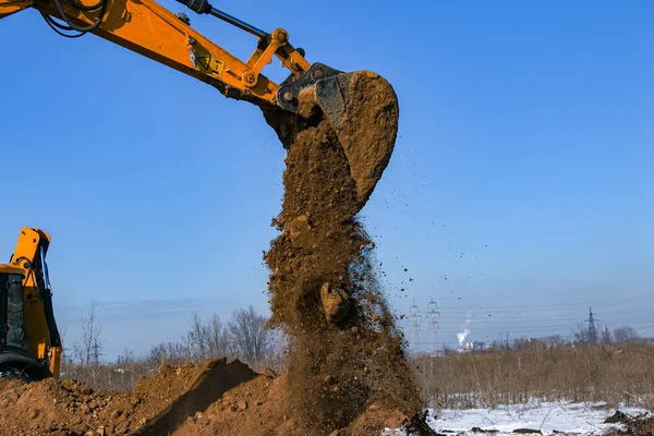 Crawler excavator. The excavator in the process of work digs out the earth and pours it onto the site. Works on a clear winter day against the blue sky.