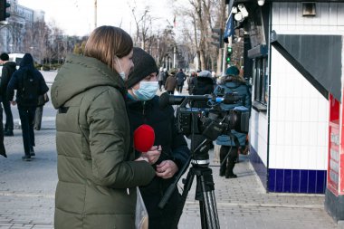 Dnepropetrovsk, Ukrayna - 03.11.2021: Genç gazeteci ve kameraman, Covid-19 salgınını veya karantina koronavirüsünü önlemek amacıyla açık havada haber yapmak için profesyonel bir video kamera kullanıyor.