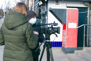 Dnepropetrovsk, Ukrayna - 03.11.2021: Genç gazeteci ve kameraman, Covid-19 salgınını veya karantina koronavirüsünü önlemek amacıyla açık havada haber yapmak için profesyonel bir video kamera kullanıyor.
