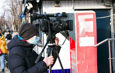 Dnepropetrovsk, Ukrayna - 03.11.2021: Genç bir kameraman, Covid-19 salgınını veya karantina koronavirüsünü önlemek için açık havada haberleri görüntülemek için profesyonel bir kamera kullanır. Tamir editör fotoğrafı.