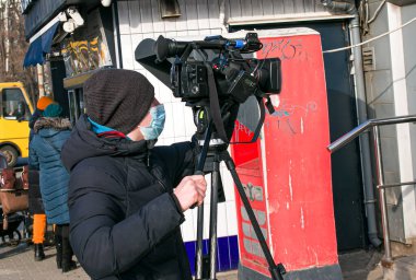 Dnepropetrovsk, Ukrayna - 03.11.2021: Genç bir kameraman, Covid-19 salgınını veya karantina koronavirüsünü önlemek için açık havada haberleri görüntülemek için profesyonel bir kamera kullanır. Tamir editör fotoğrafı.