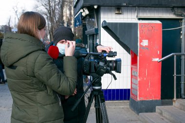 Dnepropetrovsk, Ukrayna - 03.11.2021: Genç gazeteci ve kameraman, Covid-19 salgınını veya karantina koronavirüsünü önlemek amacıyla açık havada haber yapmak için profesyonel bir video kamera kullanıyor.