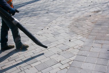 Baharın başında sokakta çalışan bir işçi hava üfleyicisiyle yaprakları ve tozu temizler. Belediye hizmetleri şehrin sokaklarını temizliyor..