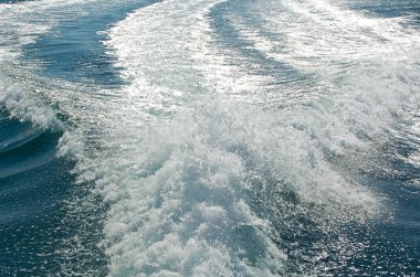 Sürat teknesinden sonra güçlü su akışı. Hızlı hareket eden motorlu teknenin arkasında su yüzeyinde iz var. Gök mavisi deniz manzarası harika. Soyut duvar kağıdı. Toprağın güzelliğini keşfedin.