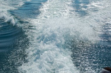 Sürat teknesinden sonra güçlü su akışı. Hızlı hareket eden motorlu teknenin arkasında su yüzeyinde iz var. Gök mavisi deniz manzarası harika. Soyut duvar kağıdı. Toprağın güzelliğini keşfedin.