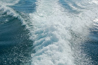 Sürat teknesinden sonra güçlü su akışı. Hızlı hareket eden motorlu teknenin arkasında su yüzeyinde iz var. Gök mavisi deniz manzarası harika. Soyut duvar kağıdı. Toprağın güzelliğini keşfedin.