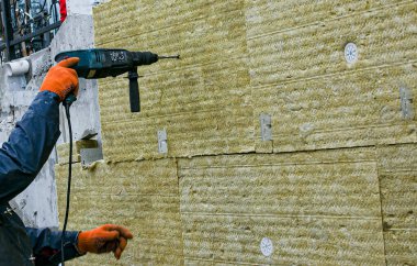 Adamın biri, dışarıdaki merdivenlerin duvarına mineral yün paneller kullanarak termal yalıtım tabakası yerleştiriyor. Dış yapıların onarımı ve yalıtımı kavramı.