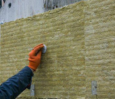 Adamın biri, dışarıdaki merdivenlerin duvarına mineral yün paneller kullanarak termal yalıtım tabakası yerleştiriyor. Dış yapıların onarımı ve yalıtımı kavramı.