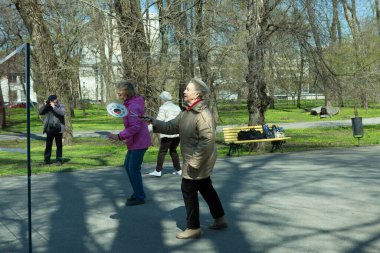 Dnepropetrovsk, Ukrayna - 04.22.2021: Parkta sağlık iyileştirici jimnastik yapan bir grup yaşlı insan. Yaşlı adamlar minitenis oynar..