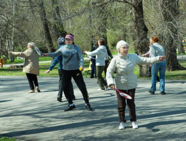 Dnepropetrovsk, Ukrayna - 04.22.2021: Parkta sağlık ve spor yapan bir grup son sınıf öğrencisi. Yaşlı adamlar tenis topu ve raket egzersizleri yapar..