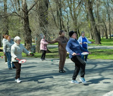 Dnepropetrovsk, Ukrayna - 04.22.2021: Parkta sağlık ve spor yapan bir grup son sınıf öğrencisi. Yaşlı adamlar tenis topu ve raket egzersizleri yapar..