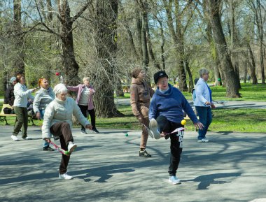 Dnepropetrovsk, Ukrayna - 04.22.2021: Parkta sağlık ve spor yapan bir grup son sınıf öğrencisi. Yaşlı adamlar tenis topu ve raket egzersizleri yapar..