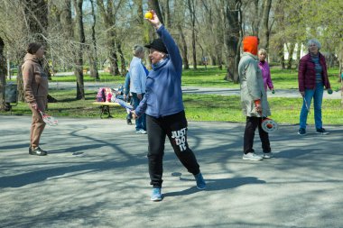 Dnepropetrovsk, Ukrayna - 04.22.2021: Parkta sağlık ve spor yapan bir grup son sınıf öğrencisi. Yaşlı adamlar tenis topu ve raket egzersizleri yapar..