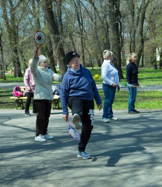 Dnepropetrovsk, Ukrayna - 04.22.2021: Parkta sağlık ve spor yapan bir grup son sınıf öğrencisi. Yaşlı adamlar tenis topu ve raket egzersizleri yapar..