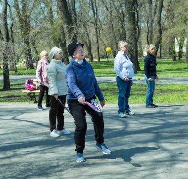 Dnepropetrovsk, Ukrayna - 04.22.2021: Parkta sağlık ve spor yapan bir grup son sınıf öğrencisi. Yaşlı adamlar tenis topu ve raket egzersizleri yapar..