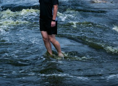 İnsanlar hızlı akan nehri geçiyorlar. Turistler sığ sularda kayaların üzerinde yürür..
