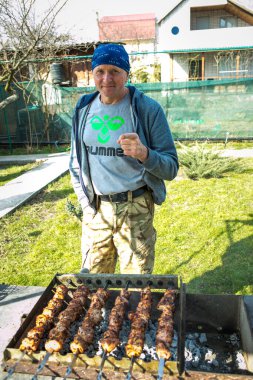 Picnic in nature. A man is grilling marinated kebabs. Close up photo of Caucasian cooking kebabs in the cottage garden.