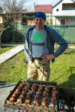 Picnic in nature. A man is grilling marinated kebabs. Close up photo of Caucasian cooking kebabs in the cottage garden.