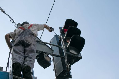 Şehir işçileri çalışan bir trafik ışığını boyuyorlar. Bir çalışan katlanan yüksek merdivende dururken tehlikeli işler yapar..