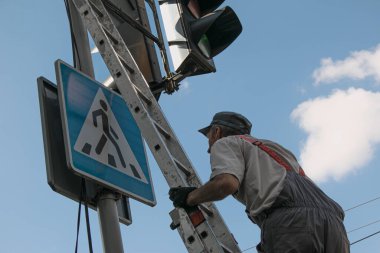 Dnepropetrovsk, Ukrayna - 05.30.2021: Şehir hizmetleri işçileri çalışan bir trafik ışığını boyuyorlar. Bir çalışan katlanan yüksek merdivende dururken tehlikeli işler yapar..