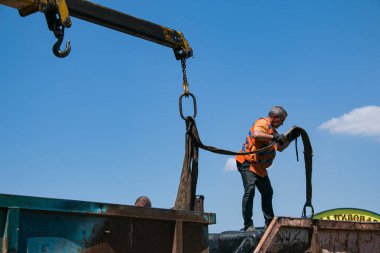 Dnepropetrovsk, Ukrayna - 05.28.2021: Çöp konteynerlerini vinç kullanarak bir kamyona yüklemek. Slinger çalışıyor..