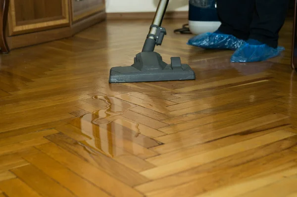 A vacuum cleaner on a wooden parquet collects spilled water - a nozzle and a vacuum cleaner close-up. Wet cleaning of parquet with a modern black vacuum cleaner.