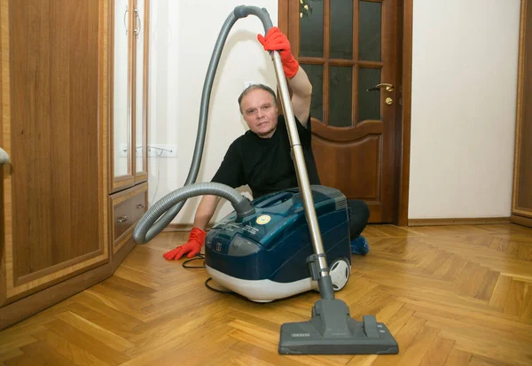 Emotions of a middle-aged man before cleaning an apartment. Daily cleaning of the premises. Humor.A man holds a vacuum cleaner in his hands.
