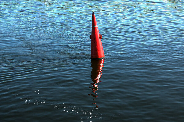 Floating red navigational buoy on blue water of Dnipro River. Buoy in the river. Navigation equipment. Tranquil water surface.