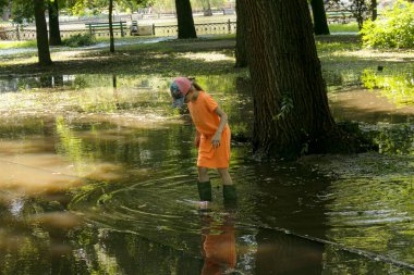 Dnepropetrovsk, Ukrayna - 06.19.2021: Sel basmış bir parkta lastik çizmeli çocuklar oynuyor.