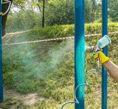 Belediyenin çalışanları parktaki bir oyun parkındaki boya borularını boyuyor. Bir balondan sprey boya.
