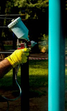 Belediyenin çalışanları parktaki bir oyun parkındaki boya borularını boyuyor. Bir balondan sprey boya.
