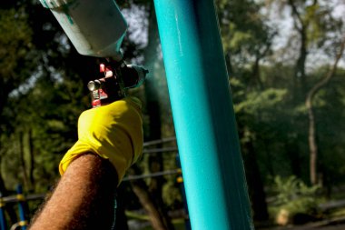 Belediyenin çalışanları parktaki bir oyun parkındaki boya borularını boyuyor. Bir balondan sprey boya.